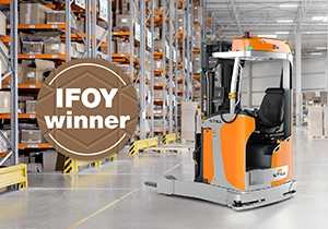 Ein orange-grauer STILL Schubmaststapler in einem Lagergang mit hohen Regalen, daneben das Siegel „IFOY winner“.