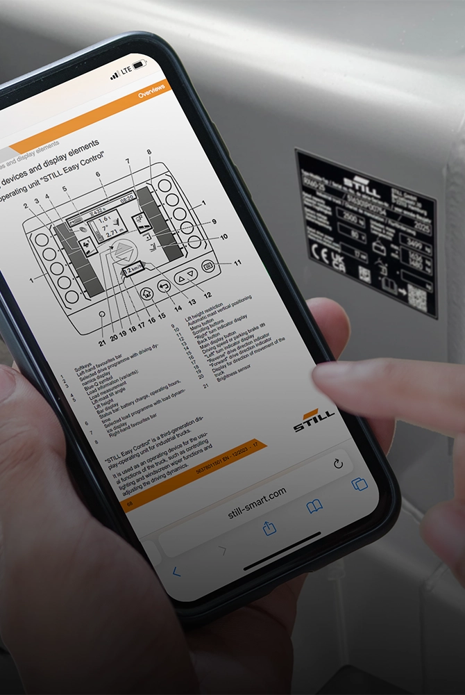 Eine Hand hält vor einem Flurförderzeug ein Smartphone, auf dem ein digitales Dokument mit einer technischen Zeichnung angezeigt wird.