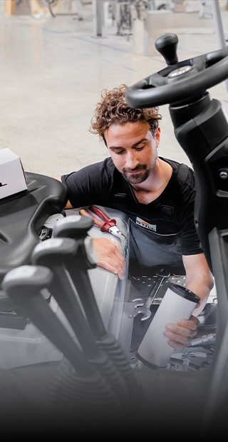 Ein STILL-Servicetechniker hält bei der Wartung eines Gabelstaplers eine Filterpatrone in der Hand, auf dem Fahrersitz steht ein STILL-Ersatzteilkarton.