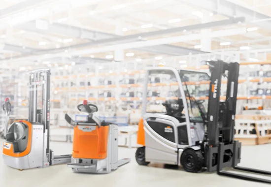 Three orange and grey STILL industrial trucks in a bright warehouse: a stacker, a pallet truck and a forklift.