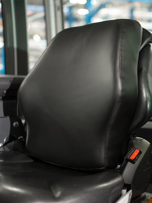Close-up of a black upholstered driver’s seat in a forklift cab, with a red seat belt buckle.