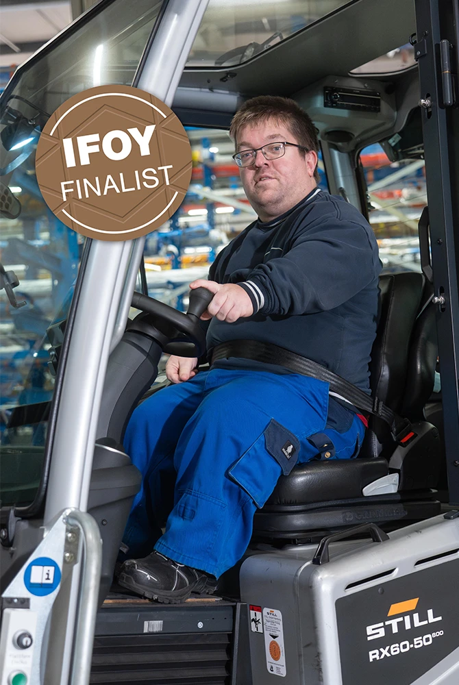 A man with glasses, wearing a seat belt, sits at the wheel of a STILL RX60-50 forklift, with an “IFOY Finalist” badge.