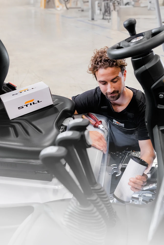 A STILL service technician holds a filter cartridge while servicing a forklift, with a STILL spare parts box on the driver’s seat.