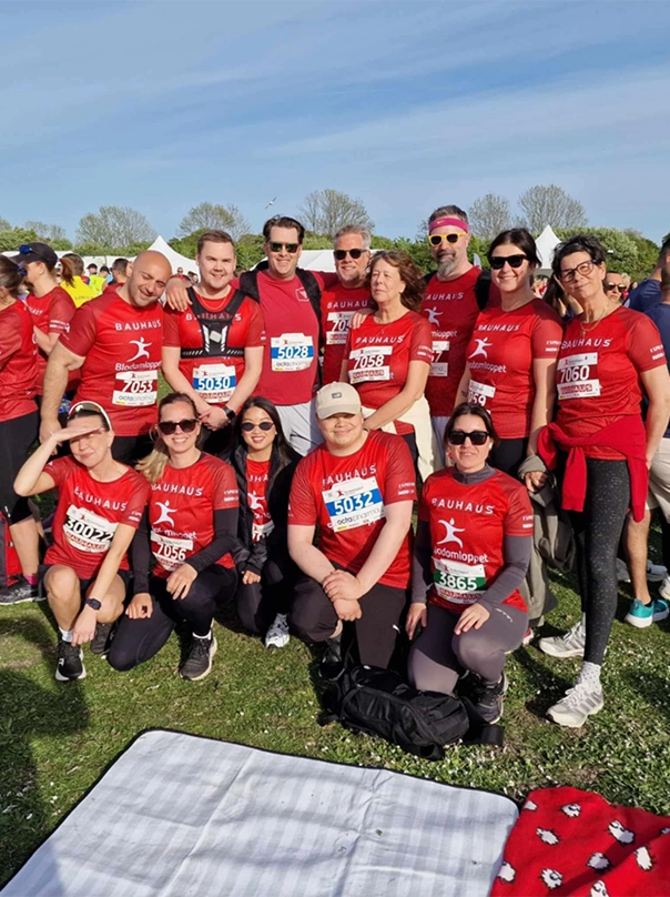 Group photo of a running team in red shirts with start numbers, on a meadow.
