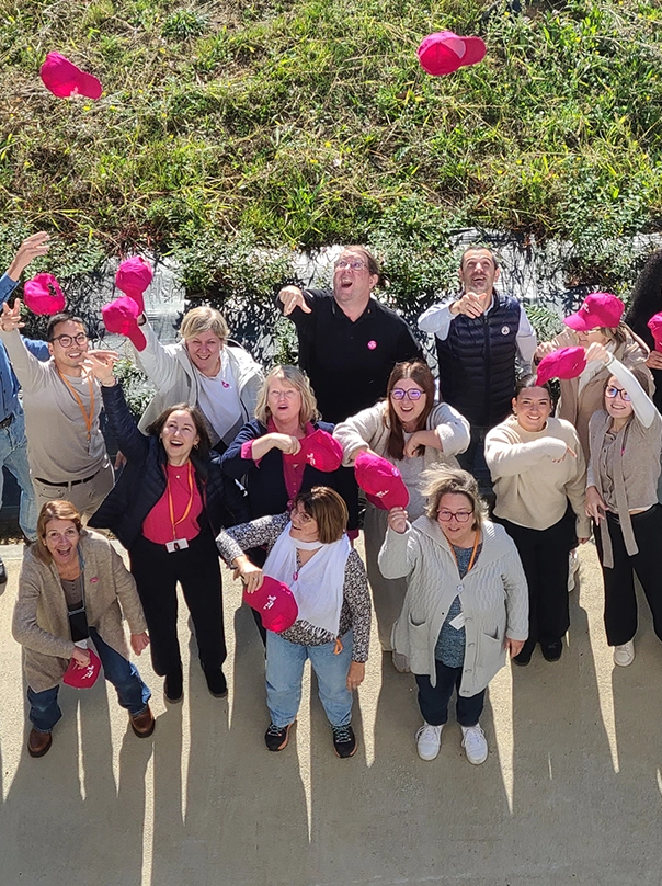 A cheerful group of employees, seen from above, throws pink caps into the air.